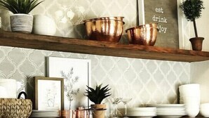 A kitchen with a patterned backsplash, copper cookware on shelves, and utensils hanging on the wall.