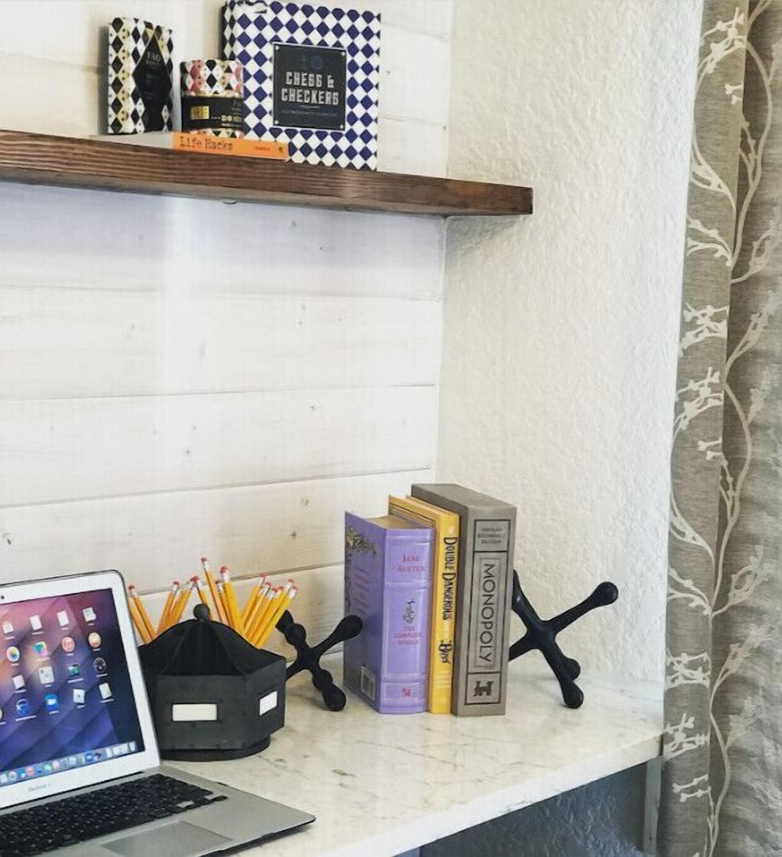 A desk with a laptop, books, a pencil holder, and a Monopoly game.