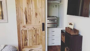 A room with a wooden sliding door, a white dresser, a television on the wall, and a bed with a gray blanket.