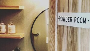 A powder room with a wooden wall, a shelf with jars, and a sign that reads "POWDER ROOM". - Cut Bank Studio #6 near Glacier National Park (Cut Bank)