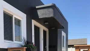 Ein modernes Haus mit dunkler Fassade, einer Holzterrasse und einer Treppe, die zur Haustür führt.