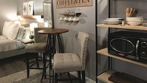 Ein gemütliches Wohnzimmer mit Schild für Kaffee und Tee, ein Essbereich mit kleinem Tisch und Stühlen sowie eine Küchenzeile mit Mikrowelle und Regalen.