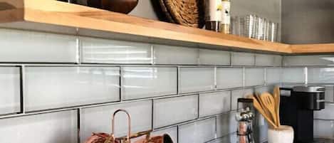 A kitchen with a black countertop, copper mugs hanging on a rack, a woven basket, and a bottle on a wooden shelf.