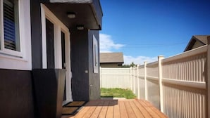 Una terraza de madera con una valla blanca y una casa al fondo.