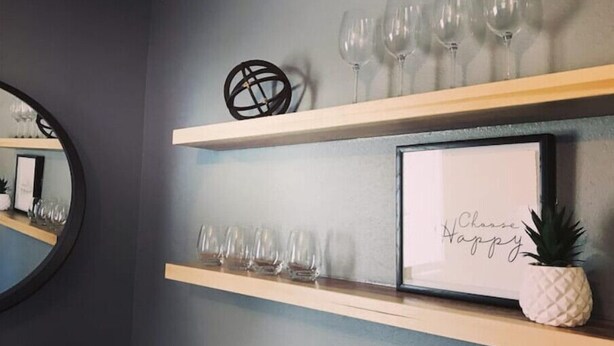 Een muur met twee houten planken waarop wijnglazen en een ananas staan.