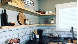 Una cocina moderna con encimeras negras, un lavamanos de acero inoxidable y estantes de madera sobre la encimera.