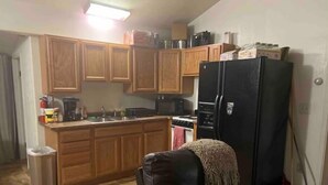 A compact kitchen with wooden cabinets, a black refrigerator, and a small island. - Chena marina guest apartment.  (Fairbanks)
