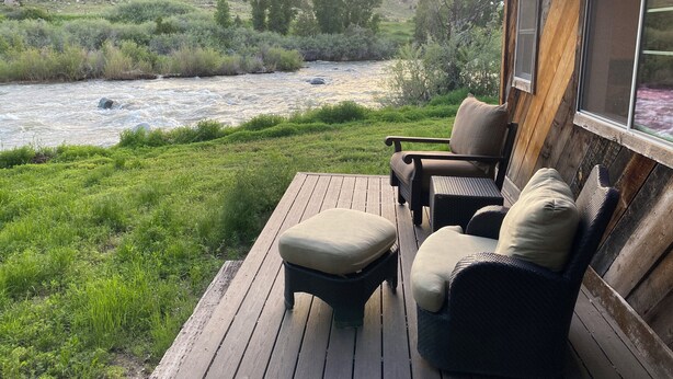 A wooden deck with outdoor furniture overlooking a river and hills.