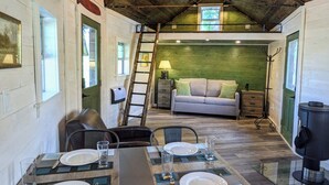 A dining area with a long table set for four, a sofa in the background, and a wooden ceiling.