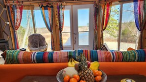 Una habitación con un sofá de rayas coloridas, una mesa con un frutero y un gato sobre una silla.