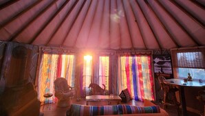Interior de una yurta con una zona de estar central, una mesita pequeña y cortinas coloridas.