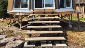 Un pabellón de madera con techo curvo y ventanas amplias, sobre una base también de madera con escalones que conducen a él.