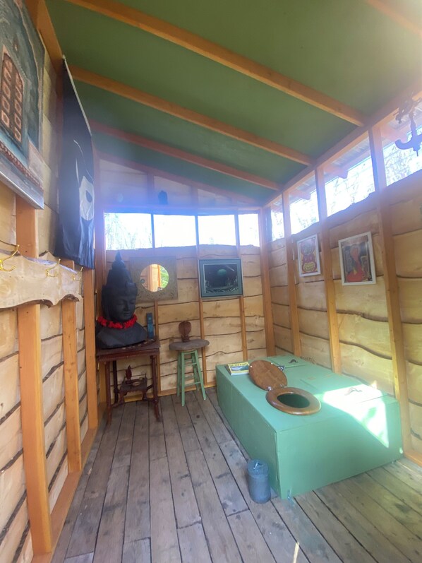 A rustic wooden cabin with a small table, a stool, a green bench, and a wooden toilet. - Sky high yurt with amazing view of the river (Baddeck)