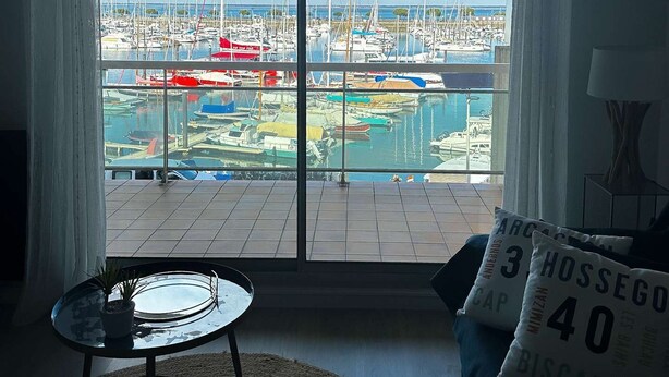 A living room with a large sliding glass door leading to a marina view. - T2 moderne avec vue bassin – 4 couchages (ARCACHON)