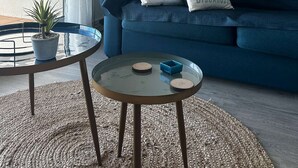 A modern living room with a blue sofa, two decorative pillows, a small round table, a potted plant, and a framed picture on the wall. - T2 moderne avec vue bassin – 4 couchages (ARCACHON)