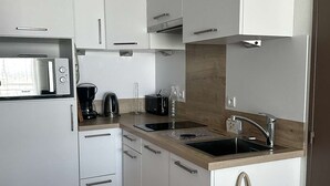A modern kitchen with white cabinets, a microwave, a coffee maker, and a sink. - T2 moderne avec vue bassin – 4 couchages (ARCACHON)