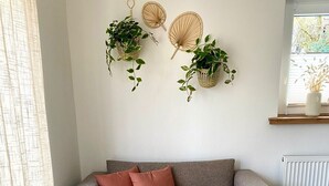 Uma sala de estar acolhedora com um sofá cinzento, duas mesas de centro redondas de madeira com plantas, um tapete cinzento e fofo e um radiador branco.