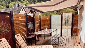 Um deck de madeira com espreguiçadeiras e uma mesa, cercado por um cercado de madeira e uma parede decorativa.