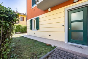 Un bâtiment avec une porte verte, un petit jardin et un chemin menant à l’entrée.