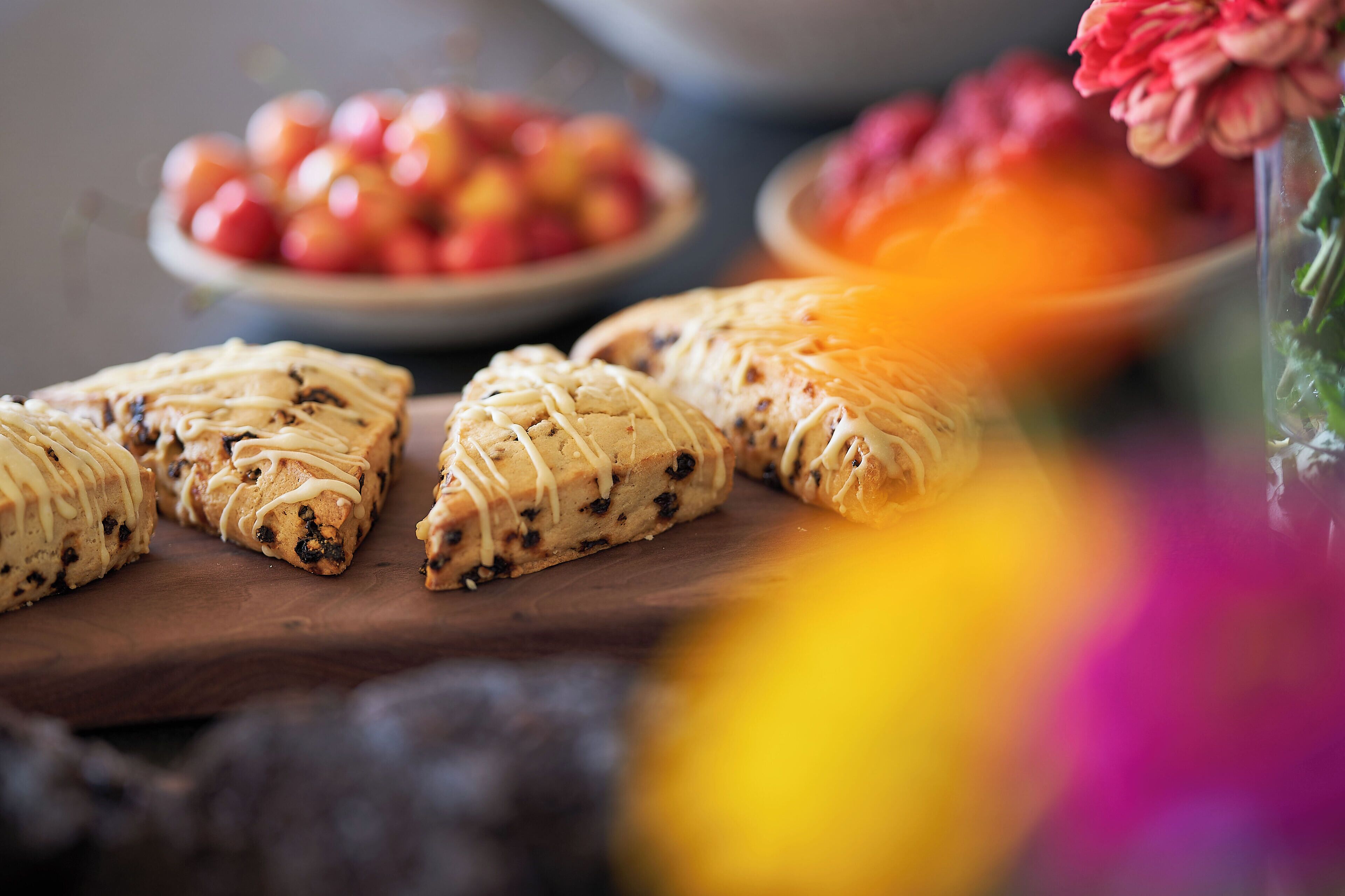 A wooden board with pastries and a bowl of fruit in the background.