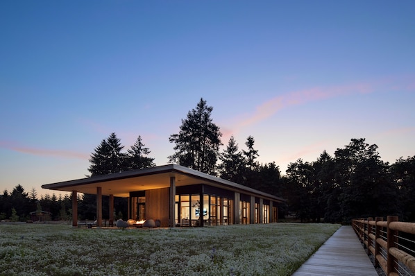 A modern house with a covered patio, surrounded by a garden and tall trees.