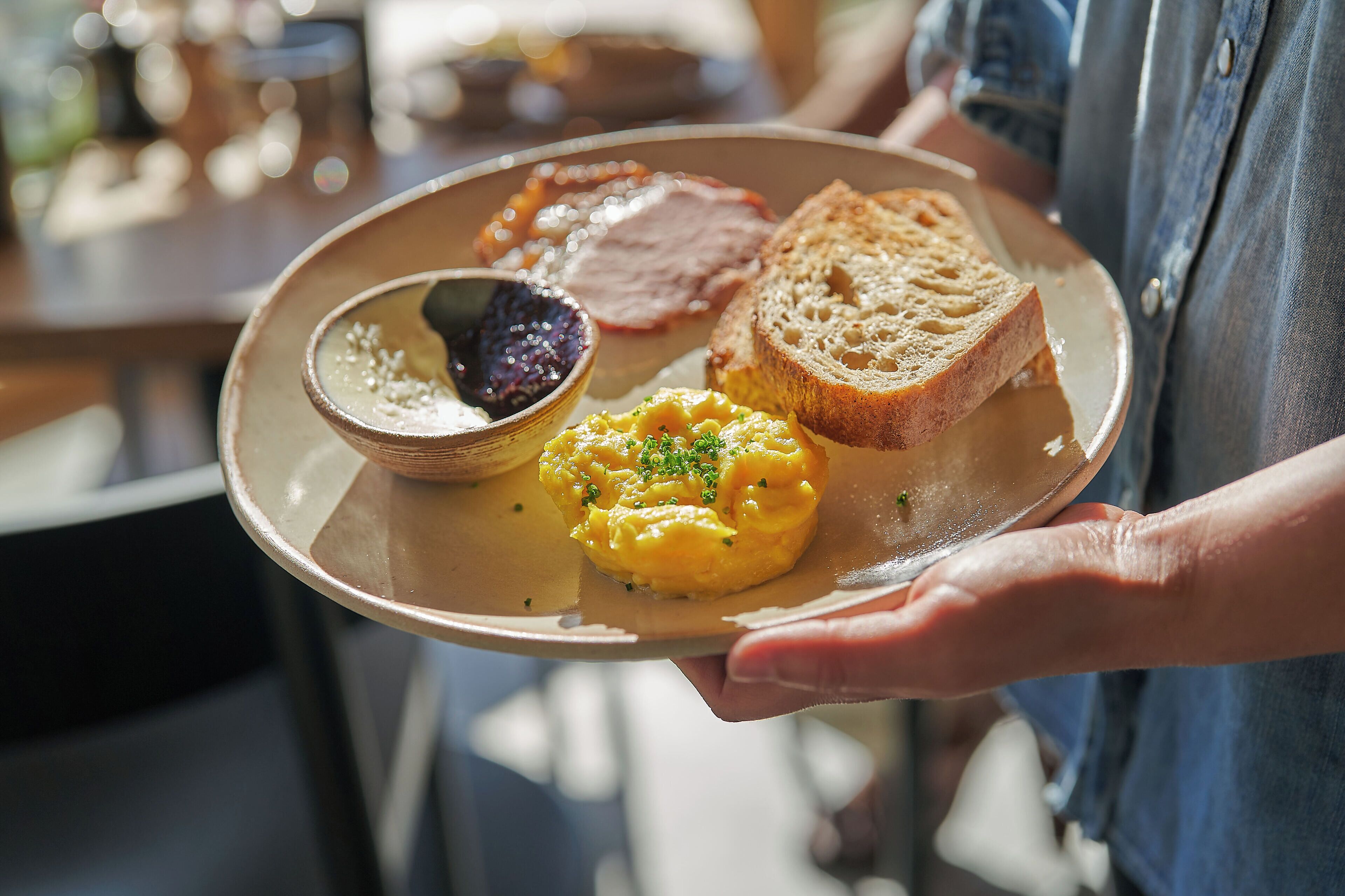 A person holding a plate with scrambled eggs, toast, and a small bowl of jam.