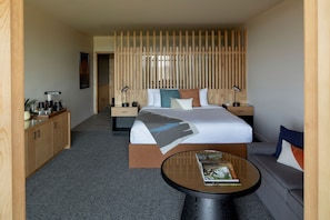 A hotel room with a bed, bedside tables, a sofa, a coffee station, and a small table with a book.