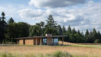 A modern house with a large open patio, surrounded by a natural landscape and tall trees.