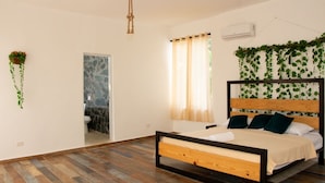 A bedroom with a wooden bed, a bathroom with a marble wall, and hanging plants. - Villa Boho Chic (Juan Dolio)