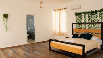 A bedroom with a wooden bed, a bathroom with a marble wall, and hanging plants.