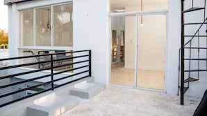 A modern building with a glass door entrance, a staircase with a metal railing, and a concrete floor. - Villa Boho Chic (Juan Dolio)