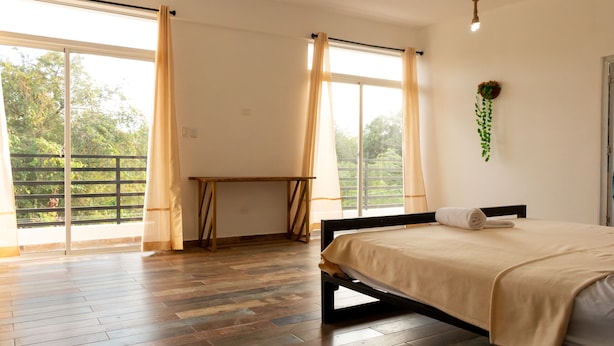 A bedroom with a bed, a desk, and a view of greenery outside. - Villa Boho Chic (Juan Dolio)