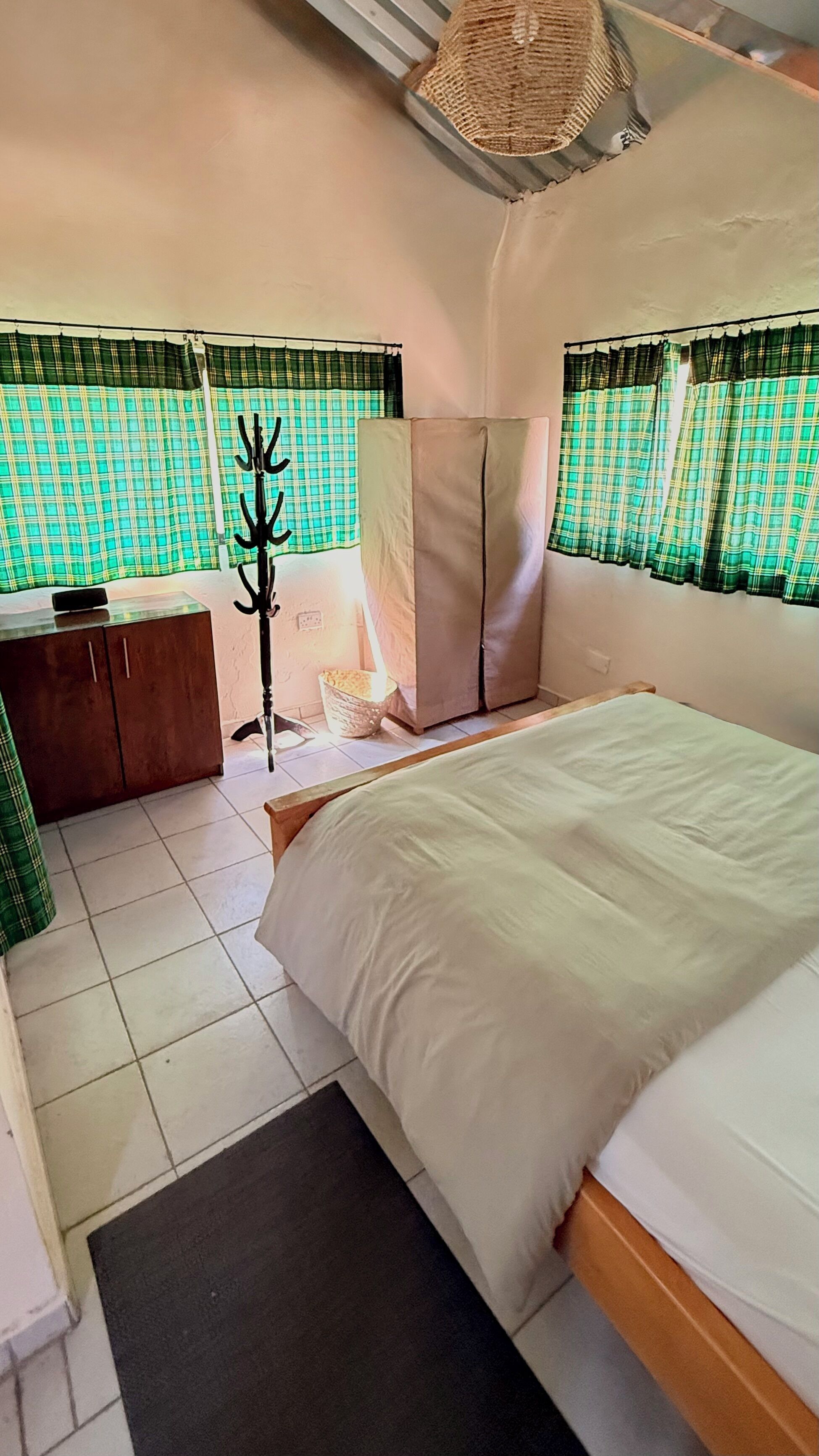 Quarto com cama, guarda-roupa, mesa de cabeceira, abajur e janela com cortinas.