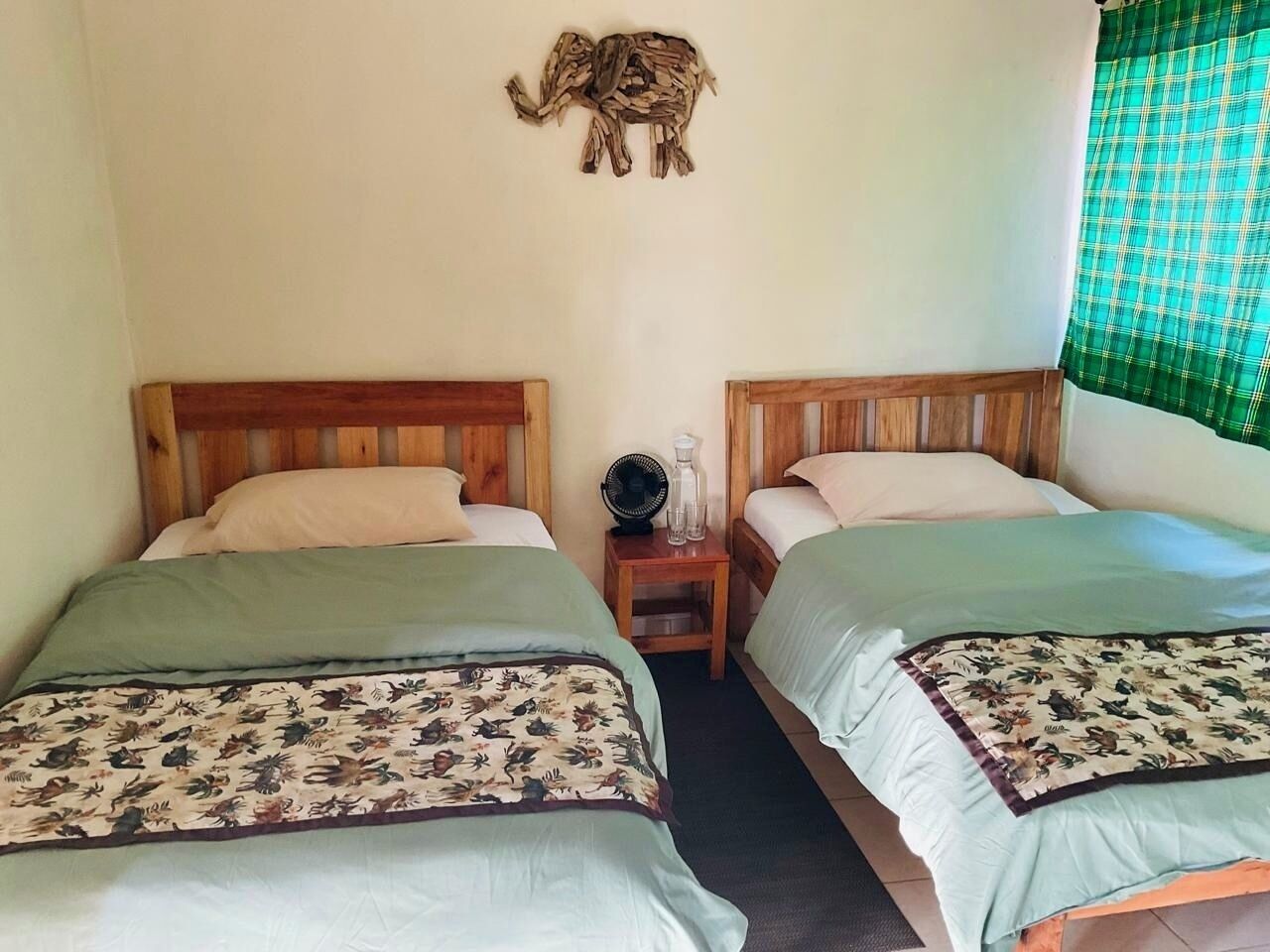 Una habitación con dos camas de madera, una mesita de noche con un ventilador y una decoración de elefante en la pared.