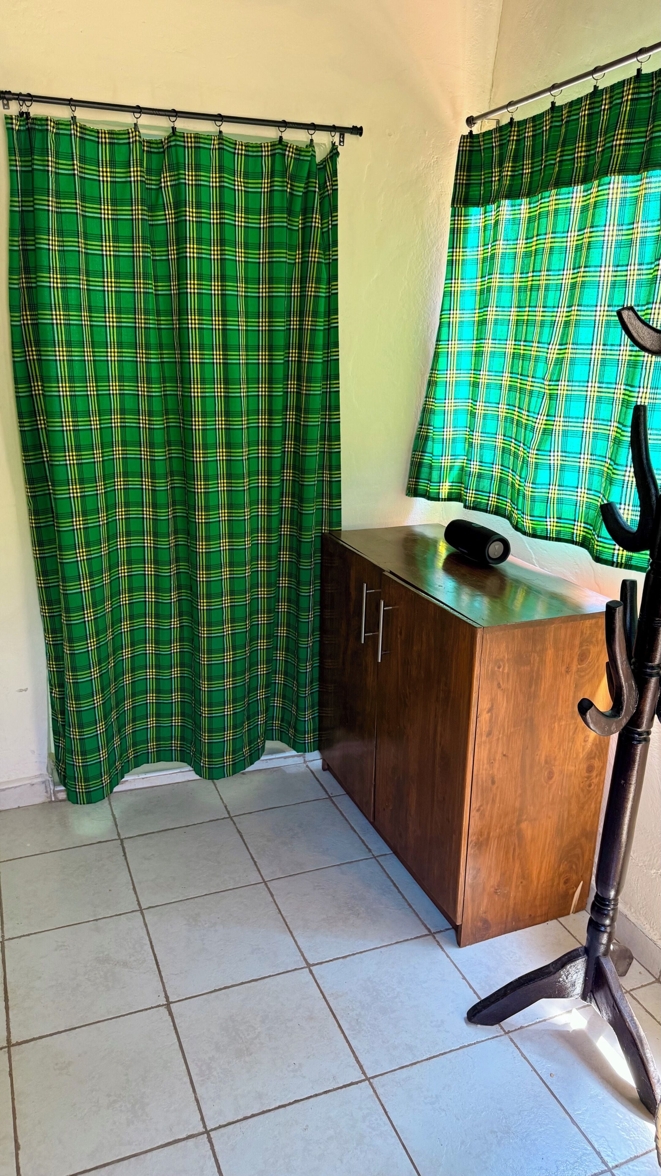 A room with a wooden cabinet, a black lamp, and green plaid curtains.