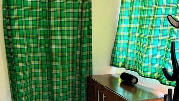 A room with a wooden cabinet, a black lamp, and green plaid curtains.