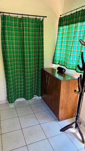 Une pièce avec un meuble en bois, une lampe noire et des rideaux à carreaux verts.