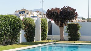 A swimming pool with a ladder, surrounded by well-maintained grass and bushes, with a building in the background. - cozy house close to the beach with garden (Saladillo Benamara)