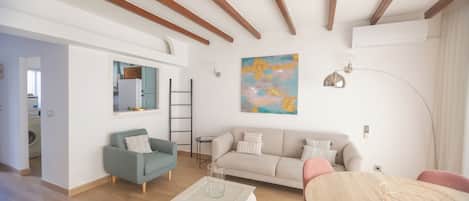 A modern living room with a sofa, coffee table, and dining table. There is a ladder against the wall and a painting above the sofa.