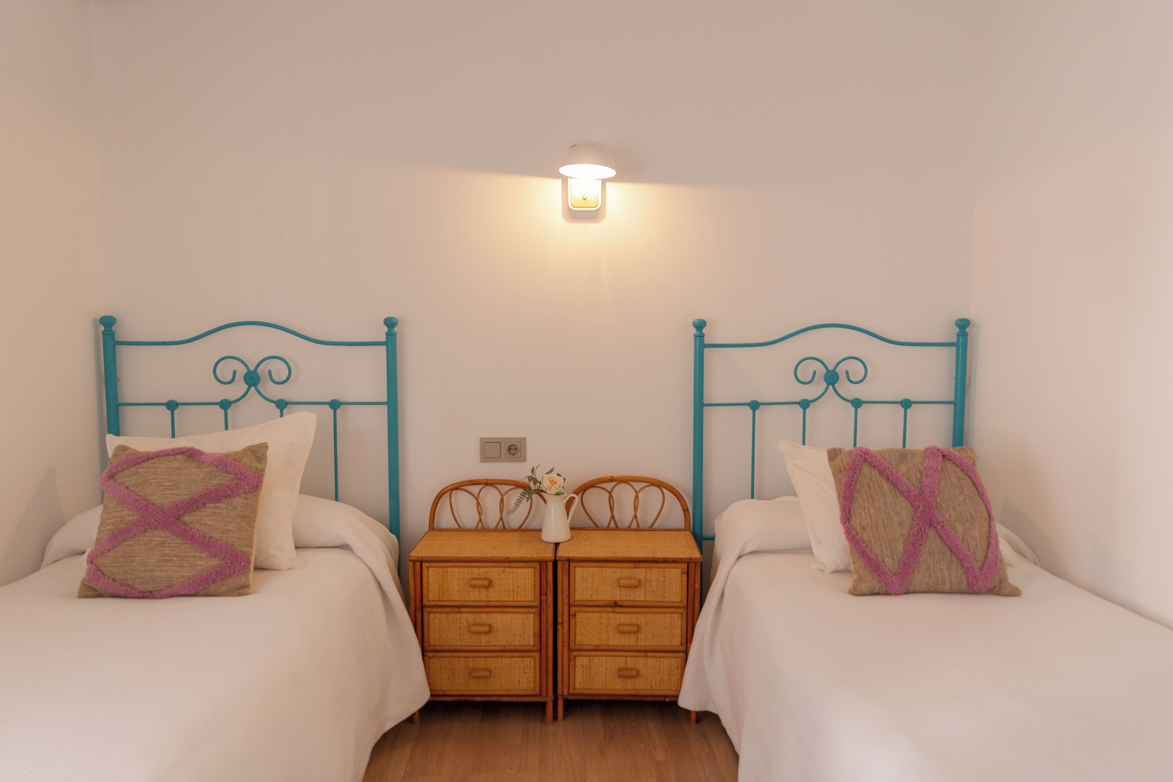 A twin bedroom with two beds, a nightstand, and a wall-mounted light fixture.