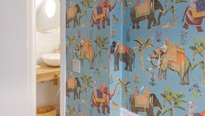 A room with a blue wall featuring a pattern of elephants and riders. There is a wooden bench with a blue bowl on it, and a white door leading to another room. - cozy house close to the beach with garden (Saladillo Benamara)