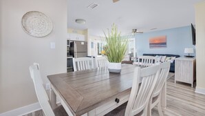 Comedor con una mesa de madera y sillas blancas, ventilador de techo y planta en maceta.