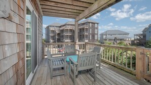 Una terraza de madera con mobiliario exterior, con vista a un barrio residencial con edificios de varios pisos.