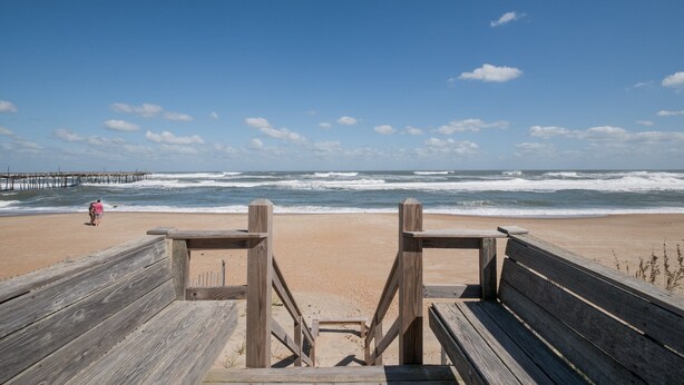 Un paseo marítimo de madera que conduce a una playa, con olas rompiendo en la orilla.
