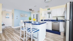 Una cocina moderna con una isla central, muebles blancos y un refrigerador de acero inoxidable.