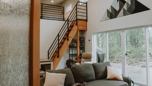 Una sala de estar moderna con un sofá gris, una escalera de madera y un ventanal con vistas al exterior.