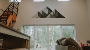 Un interior moderno con una escalera, una obra de arte geométrica en la pared y un gran ventanal que da a un área boscosa.