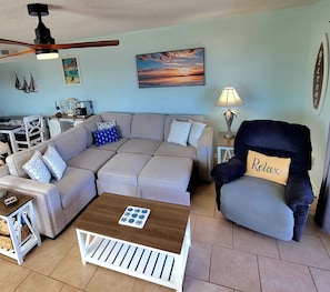 A living room with a sectional sofa, a small coffee table, a chair, a lamp, and a ceiling fan.