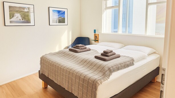 A bedroom with a bed, two framed pictures on the wall, a window, and a chair. - The Ísafjörður Inn  (Isafjordur)