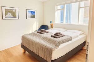 Un dormitorio con una cama, dos cuadros en la pared, una ventana y una silla.